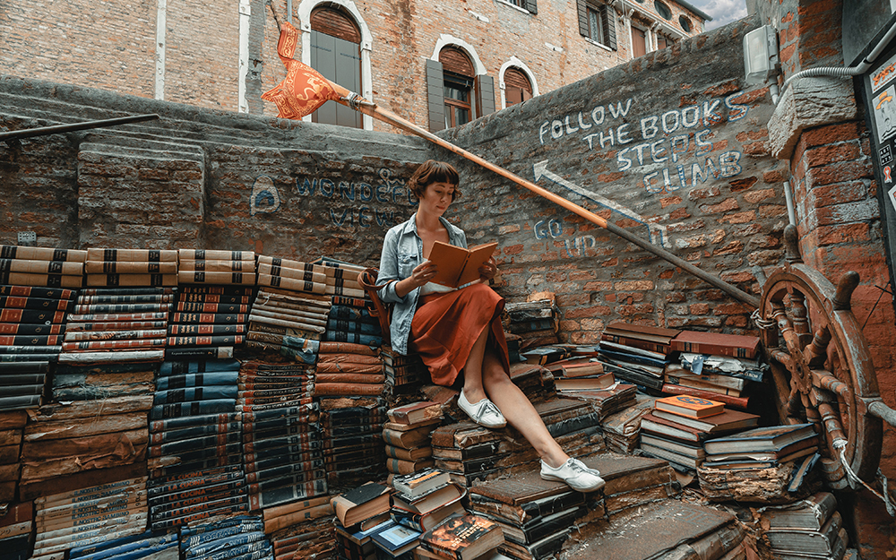 Woman sitting and reading a book on a stairway made of books