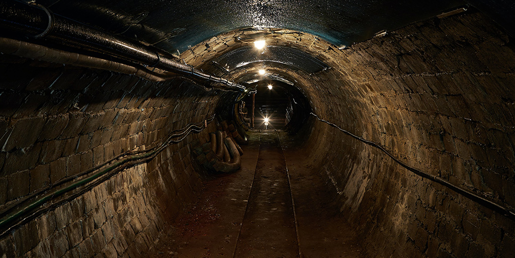 A dimly lit underground mine shaft tunnel with a tram line running down the centre